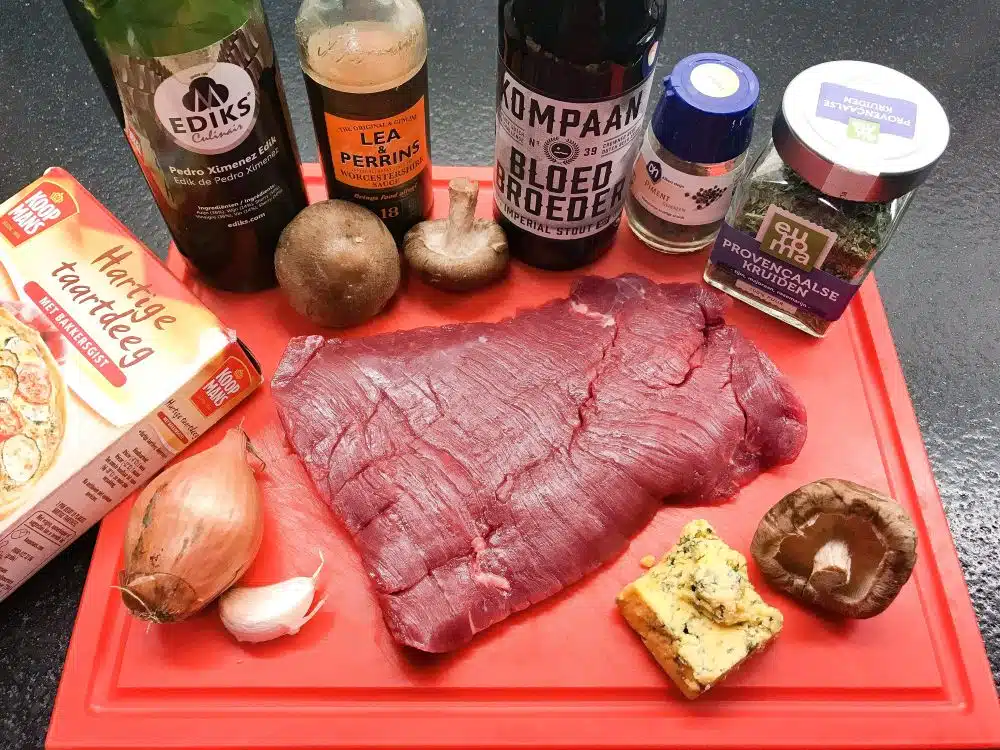 Ingrediënten (2 personen) • 200gr bavette, in reepjes van ca. 5mm • 2EL bloem • Boter om in te braden • Zout en versgemalen peper en (optioneel) een snufje pimentpoeder • 1 uitje, fijn gesnipperd • 1 knoflookteentje, fijn gesnipperd • 100gr shiitake, in plakjes • 1EL tomatenpuree • 1TL Worcestershire sauce • 1TL PX-sherryazijn • 1TL Provençaalse kruiden • 1EL basterdsuiker (optioneel) • Een klein beetje runderbouillon (ca. 150ml van bouillonblokje) of een deel runderbouillon en een deel stout-bier zoals ik deed (ik nam Kompaan Bloedbroer) • 6 vellen deeg voor hartige taart • 75gr Shropshire Blue (of een andere Engelse blauwschimmelkaas zoals Stilton), verbrokkeld • 1 eigeel, losgeklopt